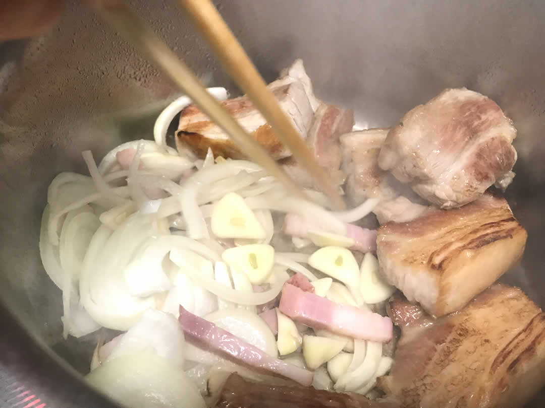 お肉に焼き目がつき脂が溶け出してきたところで、お肉を片側に寄せます。フライパンの空いたところでたまねぎ・にんにく・ベーコンを入れて一緒に炒めます。