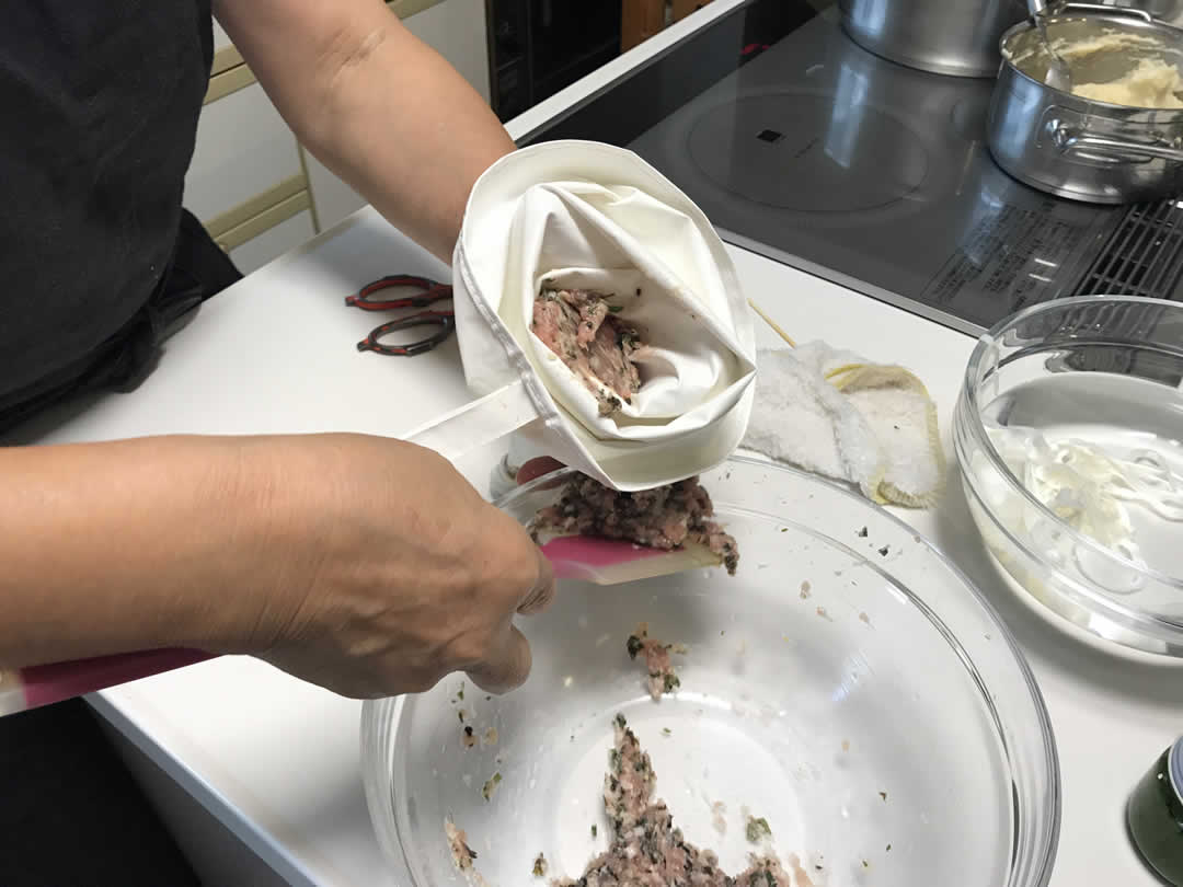 調味料と食材をよく混ぜた肉だねをへらで取り、絞り器に入れておきます。